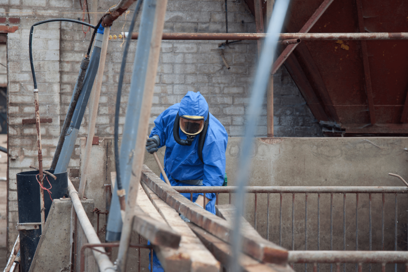 Asbestos removalist dressed in safety gear removing asbestos from a building.