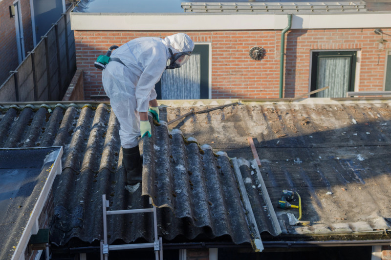 person on roof removing asbestos sheet. roof asbestos removal