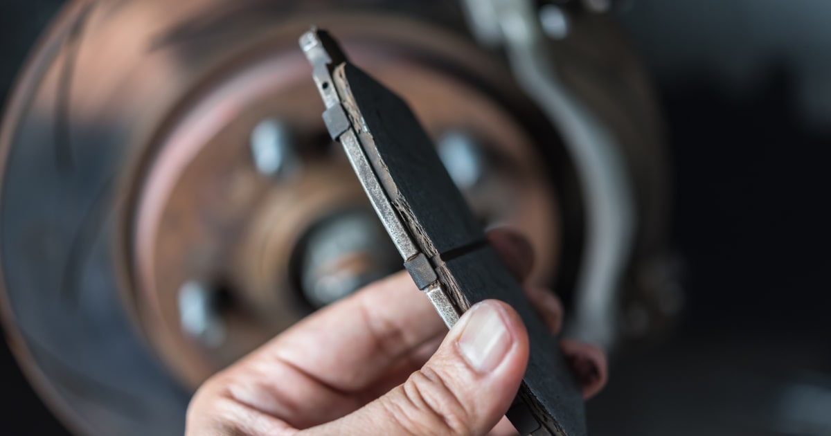 A close shot of person examining a disc brake and asbestos brake pads at car garage.