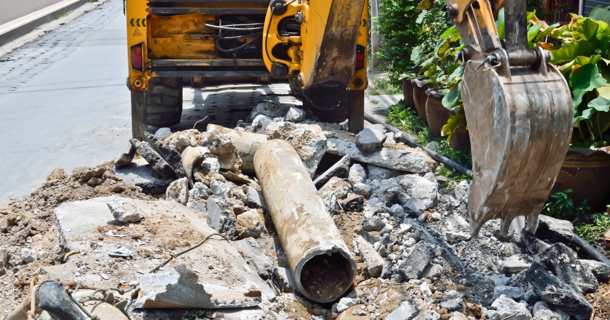 A backhoe digging with asbestos building materials and cement pipe.